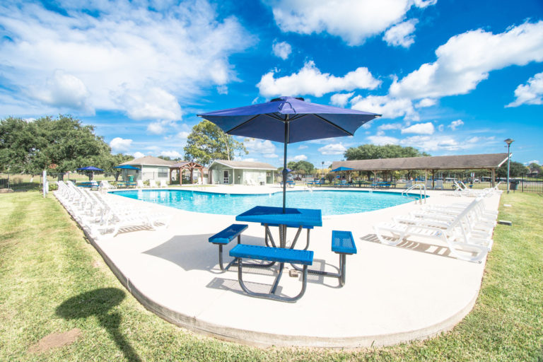 Photo of swimming pool area with lounging chairs and blue table with umbrella.
