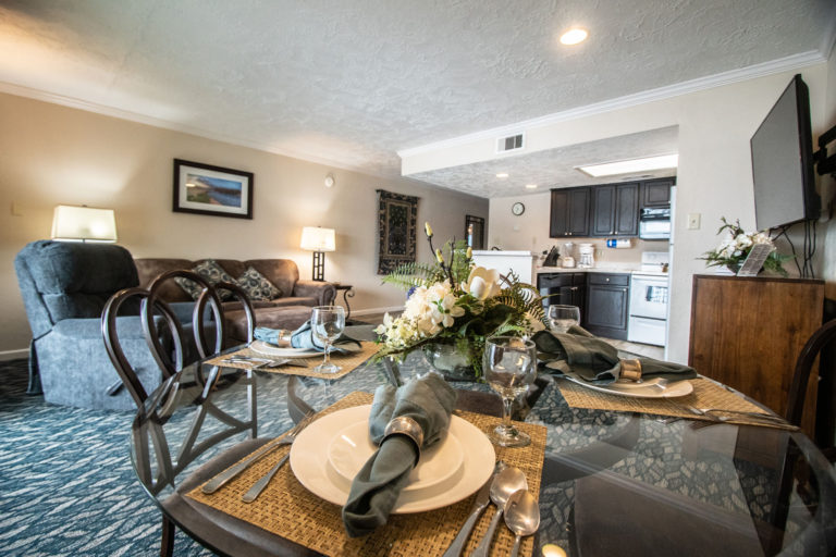 Photo of living room with arranged dining table and kitchen in the background. Unit 125