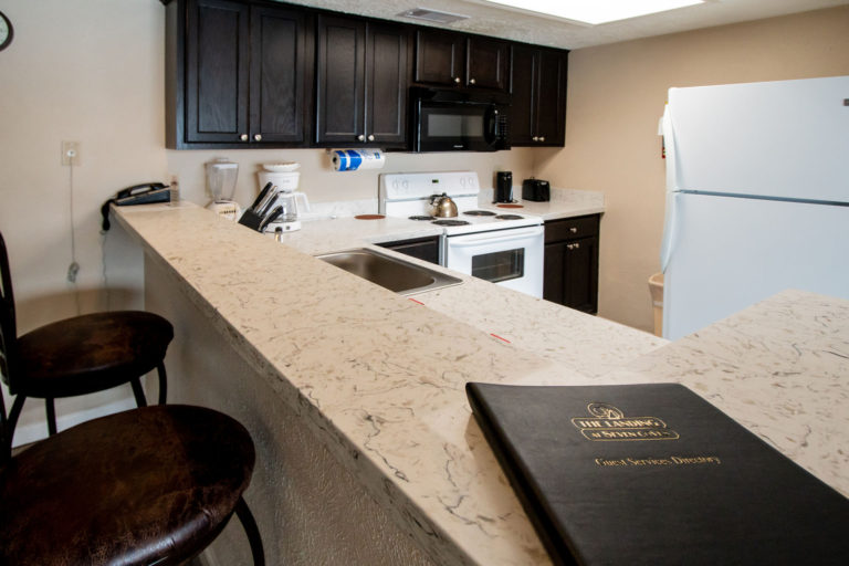 Photo of kitchen with dark wooden cabinets, white stove and black microwave. Unit 125