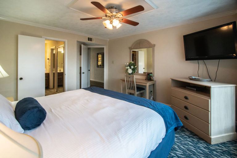 Photo of bedroom with king bed, TV, ceiling fan, mirror and drawer. Unit 125