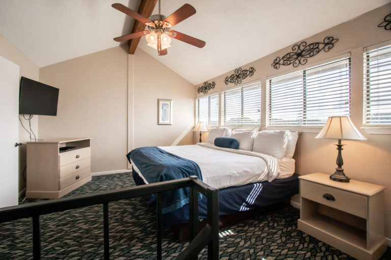 Photo of bedroom with king bed, nightstands, ceiling fan and carpeting. Room 225